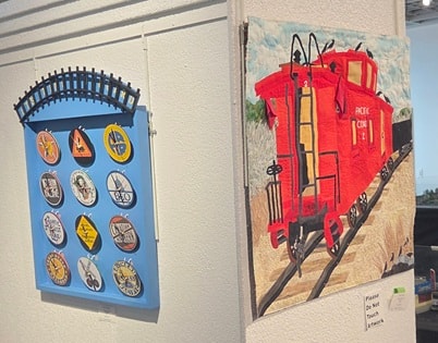 Train-related artwork on display at the gallery — train emblems and red caboose quilt