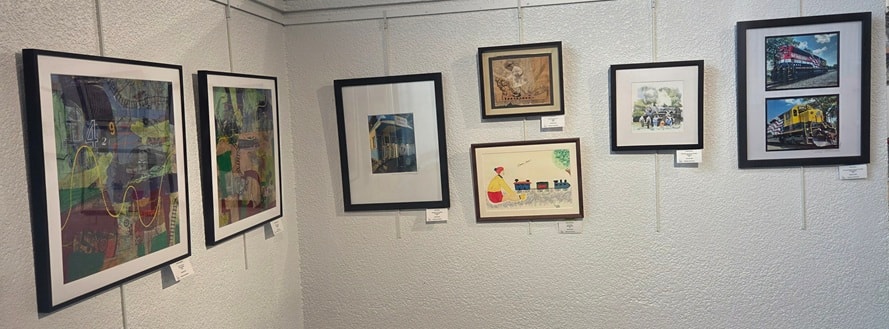 Gallery wall with train-themed framed artwork including locomotive paintings and photographs