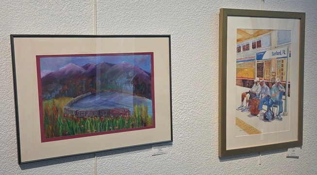 Two framed artworks — mountain train landscape and Sanford FL Amtrak station scene