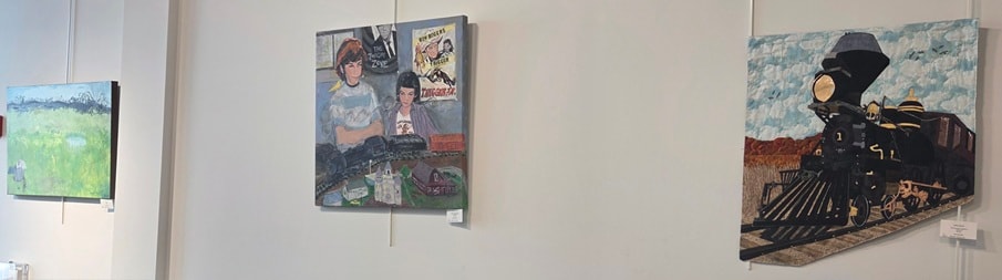 Gallery wall with paintings including a child with model trains and a large steam locomotive quilt