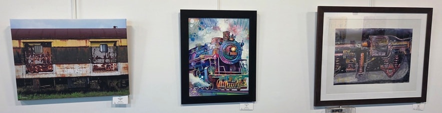 Three framed artworks — weathered rail car, colorful locomotive painting, and industrial train detail